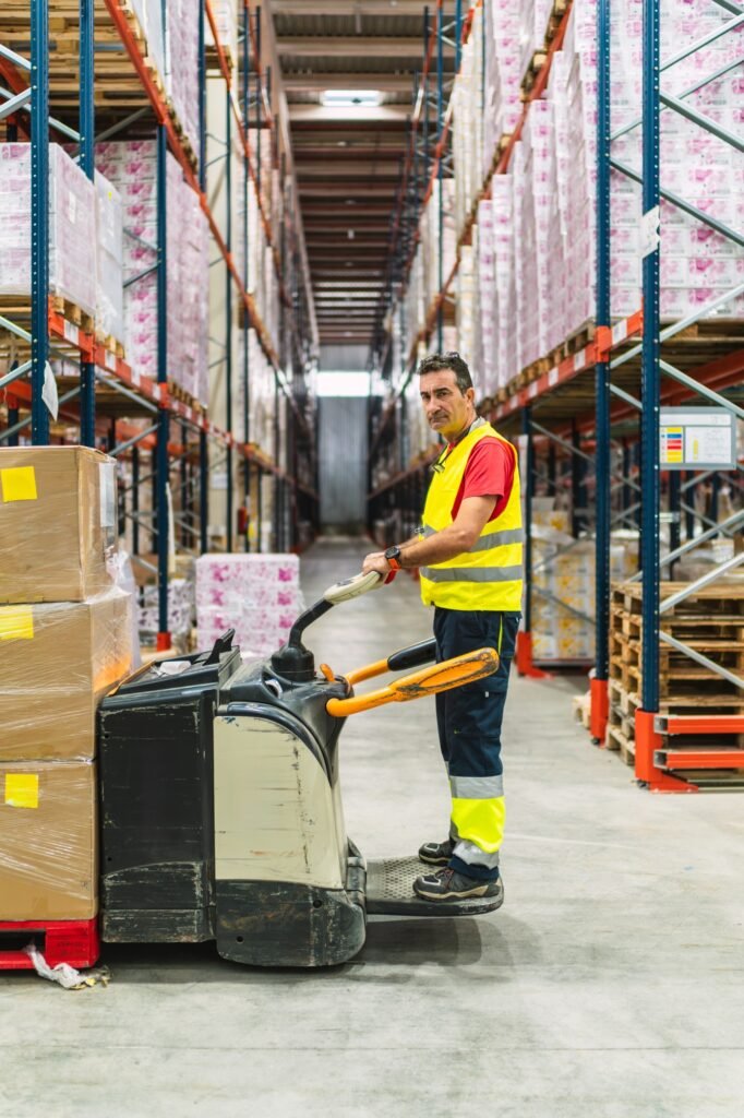 Warehouse worker moving boxes with pallet truck in logistics center